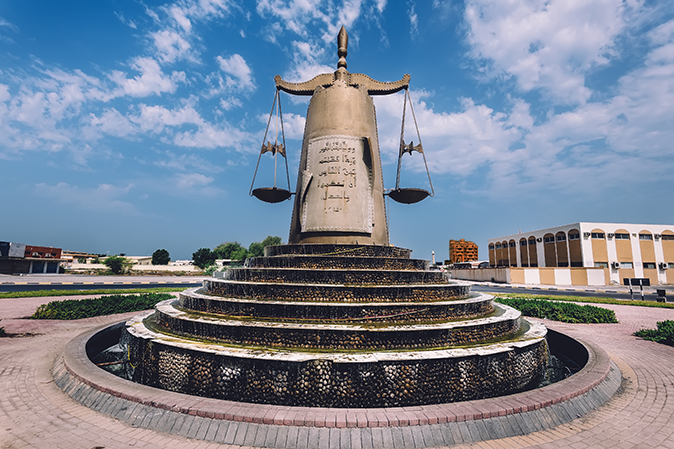 September 8, 2017 - Ras al Khaimah, United Arab Emirates. Roundabout With Scales Of Justice Statue and waterfall In Ras Al Khaimah Emirate in UAE. Traffic island with landmark on local road.