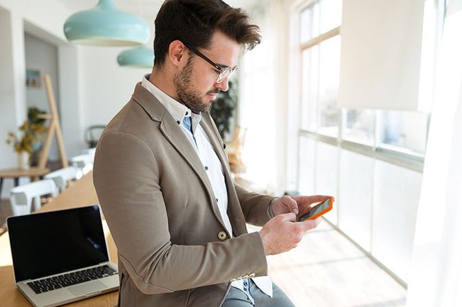 Shot of handsome young business man using his smartphone while sitting on table in the office.