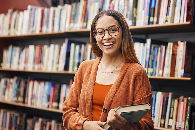 Young woman smiling while holding a book in the school library
