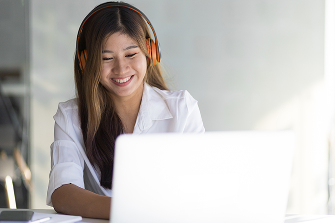 Young woman smiling while wearing headphones and typing on a laptop