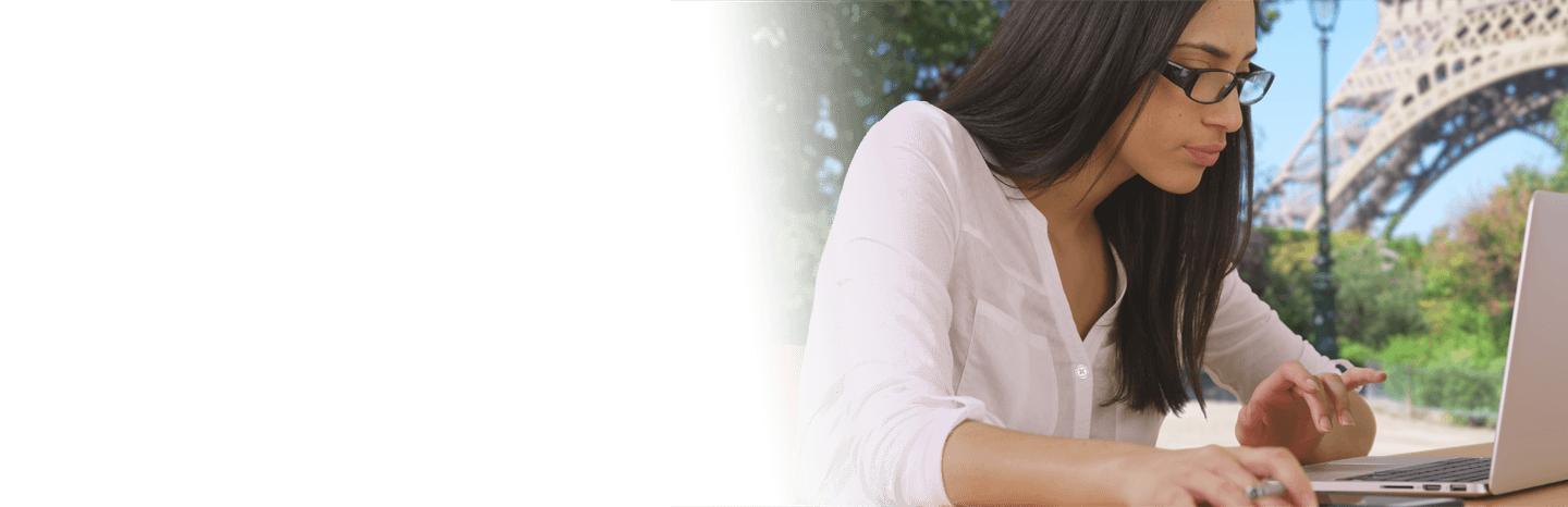 Young woman typing on a laptop outside with the Eiffel Tower in the background