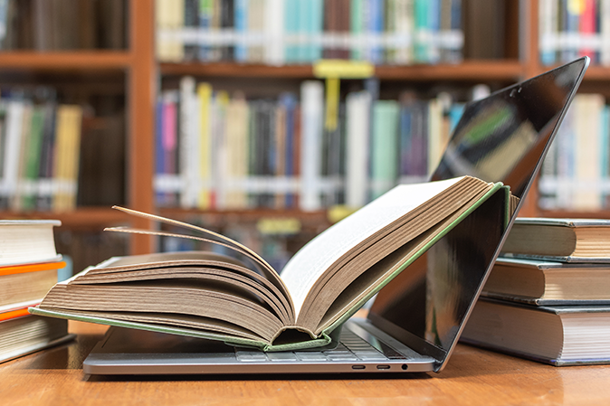 Book sitting on top of a laptop among other books in a library